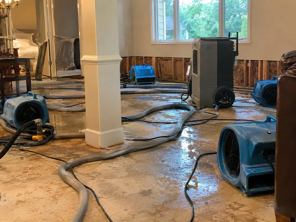 Air movers and a dehumidifier drying a room after water damage with wall sections opened